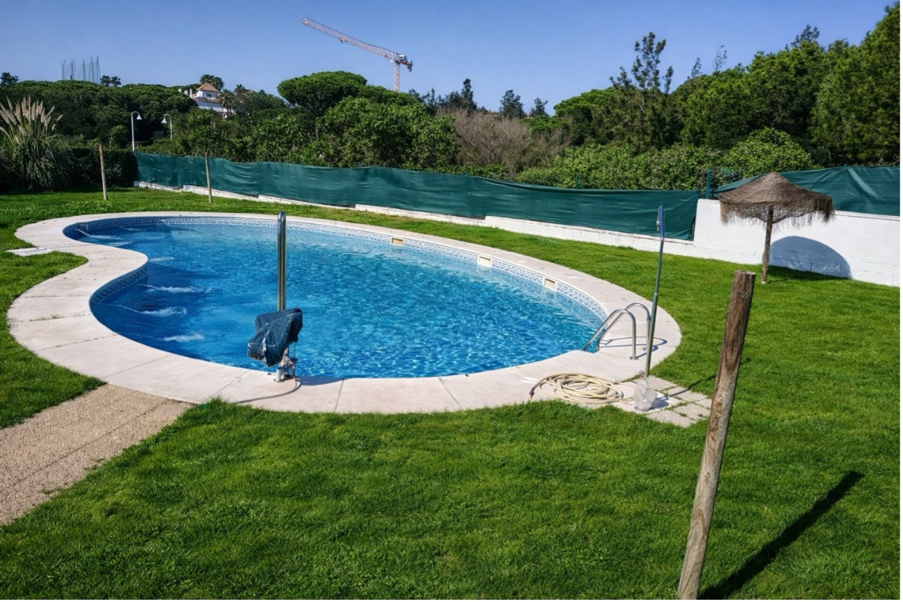 Piscina curva con zonas verdes en mantenimiento integral